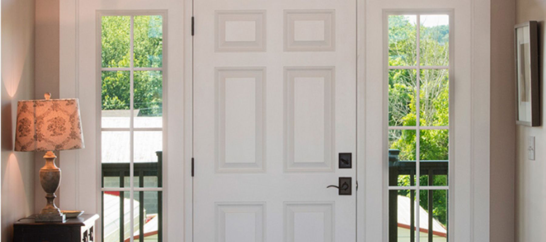 White paneled front door with narrow glass sidelights in a cozy interior entry space