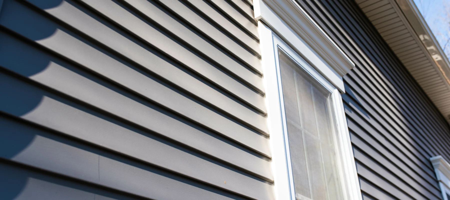 Close-up view of a house's dark blue horizontal vinyl siding and a single white-trimmed window