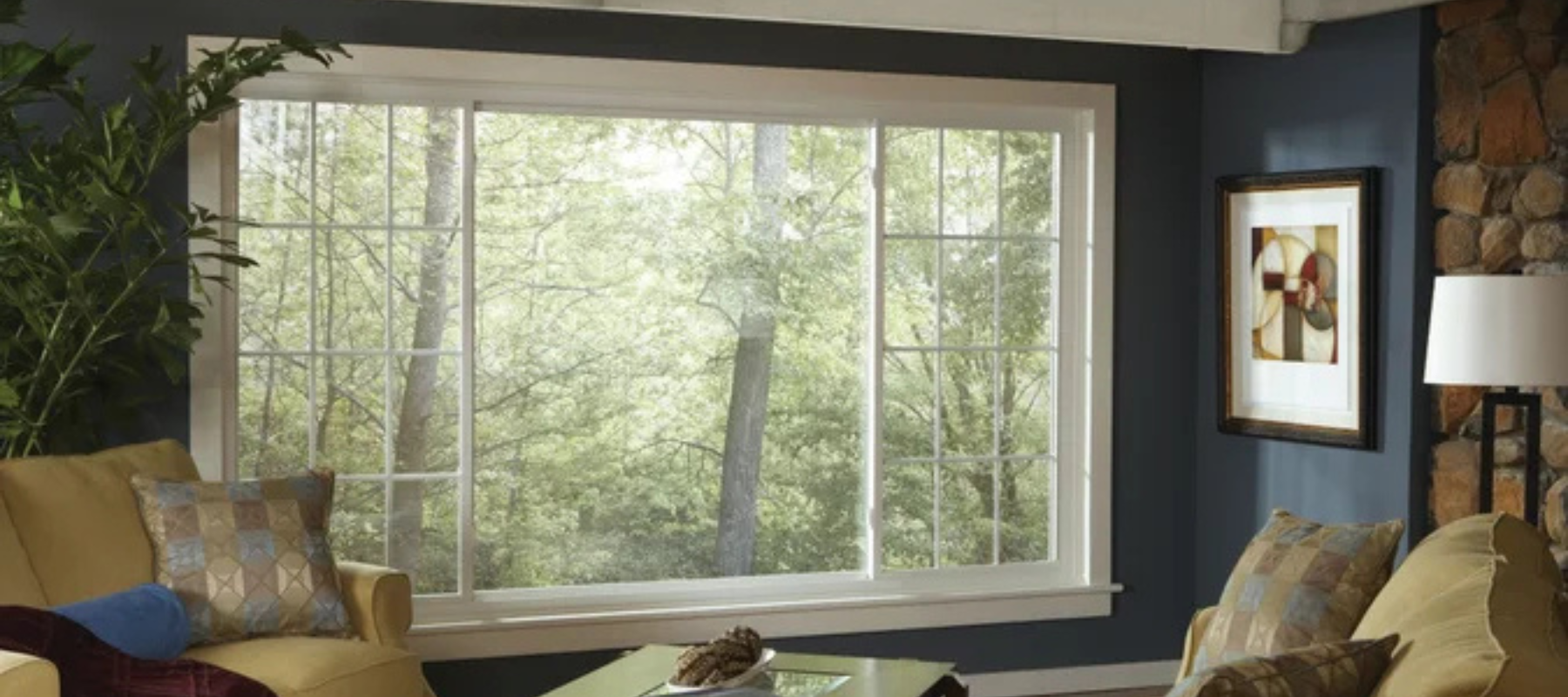 Interior view of a living room with a wide picture window showing a forested landscape outside