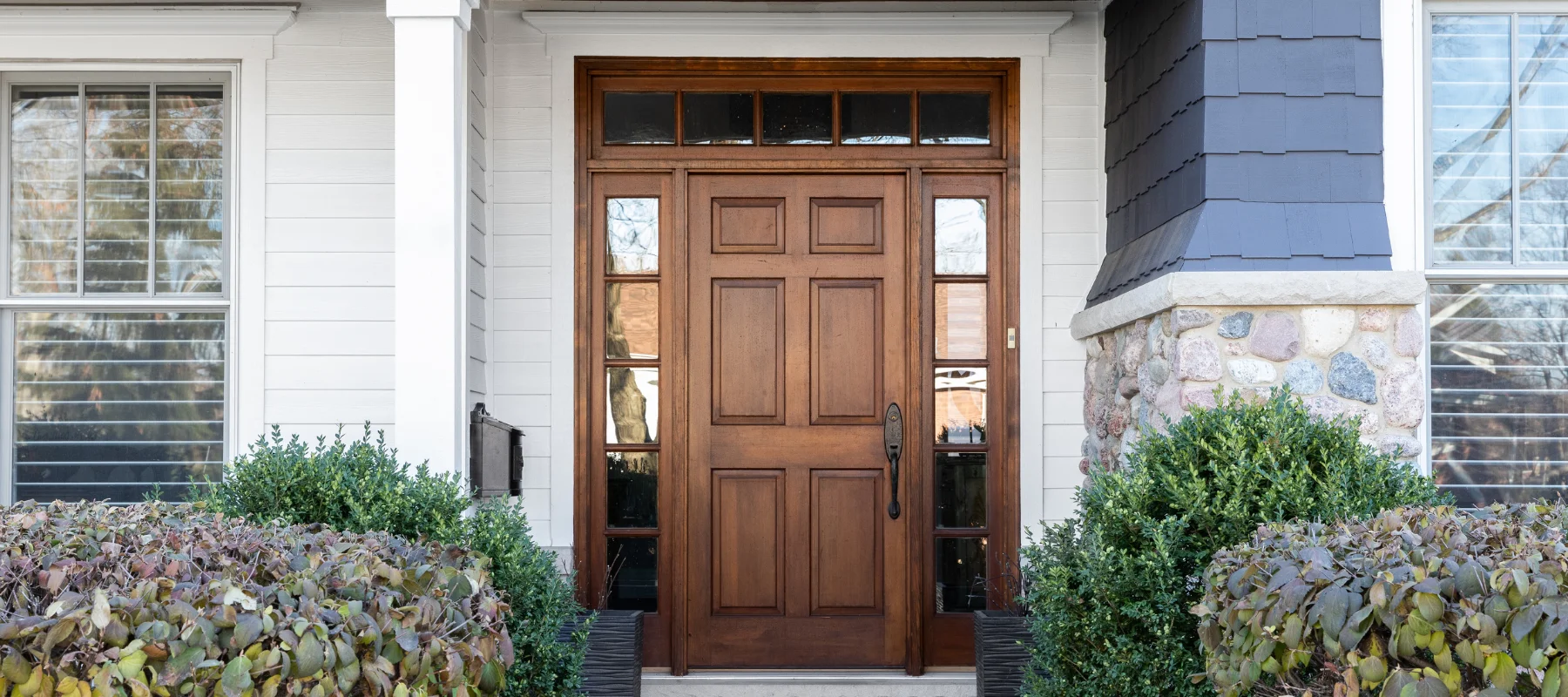 Wooden front entry door with rectangular sidelights, surrounded by stone and white siding