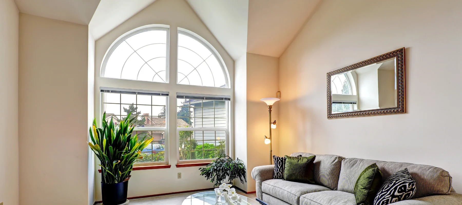 Living room with a tall arched window and transom design overlooking a residential neighborhood