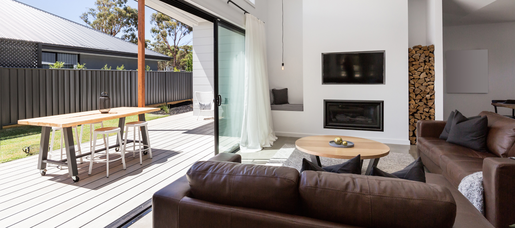 Living room with brown leather furniture and wide glass sliding doors opening to a modern patio