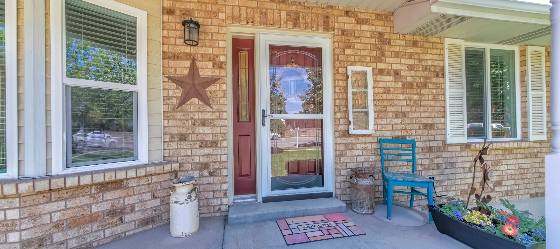 Brick porch with a red entry door and full-view storm door, accented by a star decoration and welcome mat