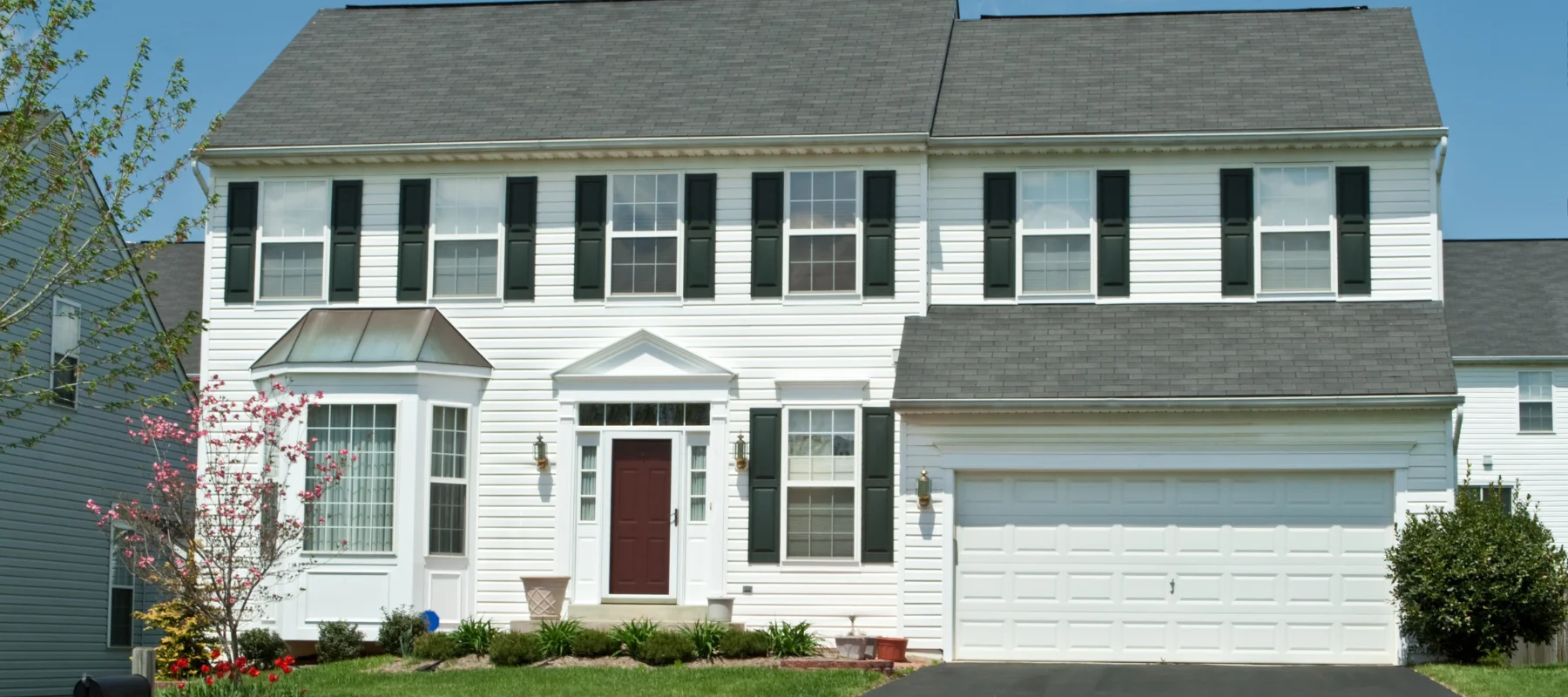 Traditional two-story house with white vinyl siding, black shutters, and a red entry door with a well-maintained lawn
