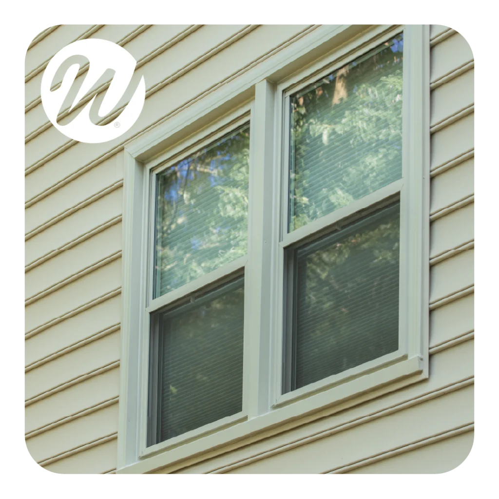 Close-up of beige double-hung window on cream vinyl siding with the Window World logo