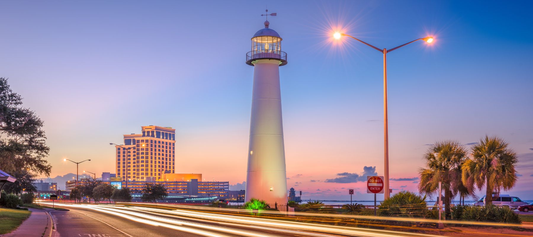 Evening view of a lighthouse near a waterfront city with streaks of car lights on the road