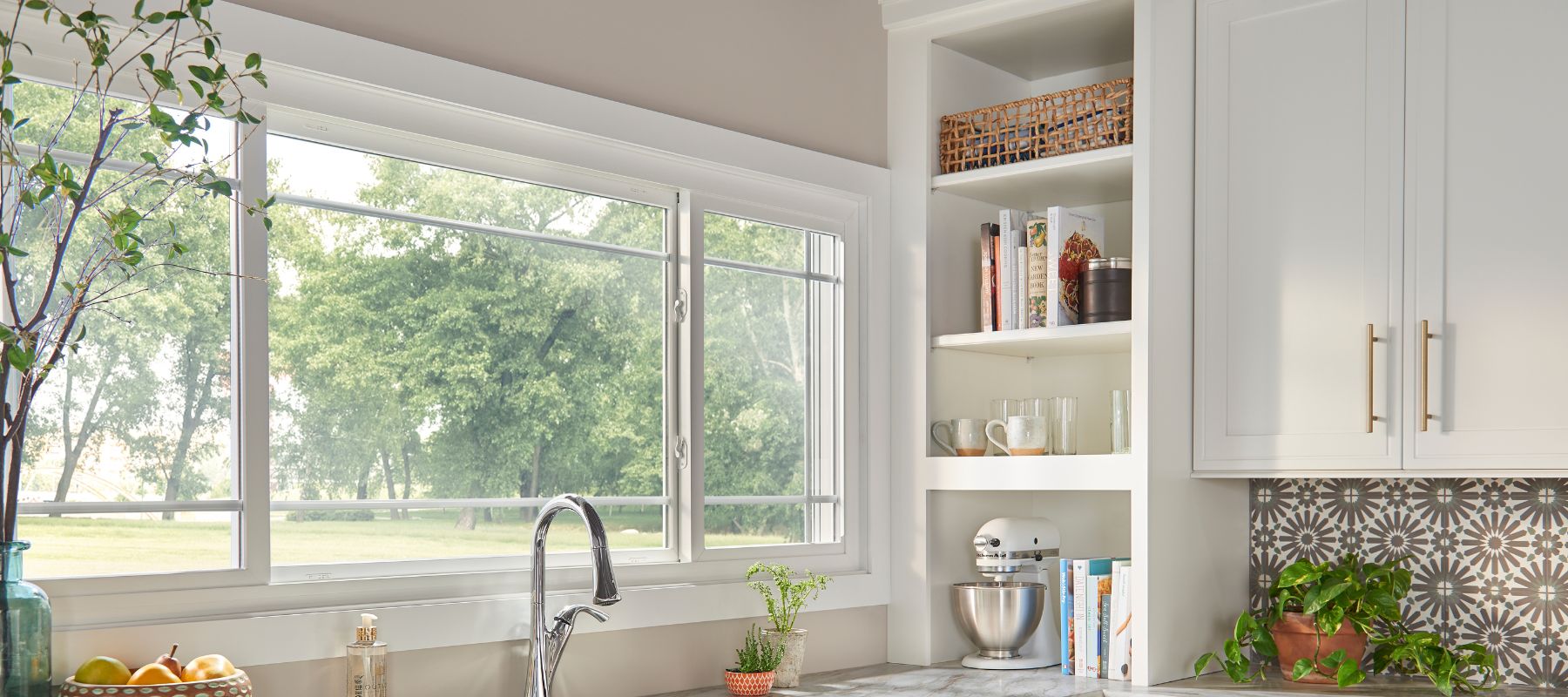 Modern kitchen with large windows, white cabinetry, plants, and kitchen appliances on the counter
