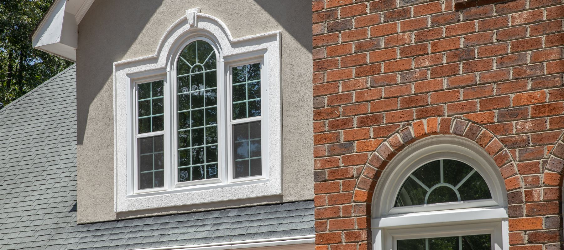 A house exterior features a mix of textures, including brick and stucco, with two prominent arched windows that have multiple white panes